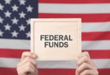 FUNDING GUILLOTINE Drops on Sanctuary Cities Person holding a sign that reads 'FEDERAL FUNDS' in front of an American flag