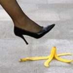 A high heel shoe poised above a banana peel on a tiled floor