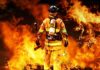 Firefighter standing in front of a large fire, equipped with tools