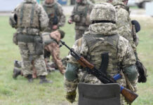 Soldiers in camouflage gear gathered on grass field.
