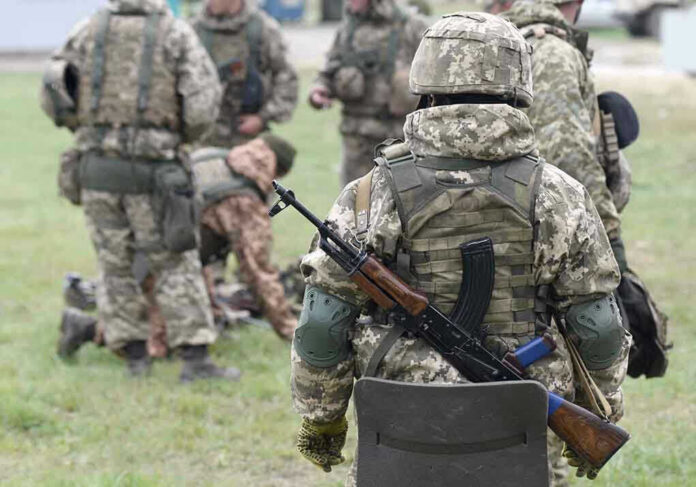 Soldiers in camouflage gear gathered on grass field.