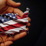 A hand holding a map of the United States adorned with the American flag