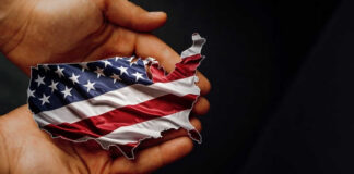 A hand holding a map of the United States adorned with the American flag