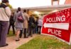 People waiting in line at a polling place with a sign indicating direction