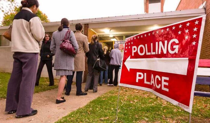 People waiting in line at a polling place with a sign indicating direction