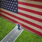 A man in a suit standing in front of a large American flag painted on a wall