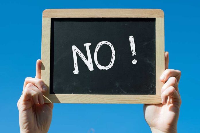 A hand holding a chalkboard with the word NO written on it against a blue sky