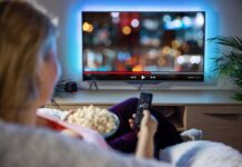 Person sitting on a couch watching a movie on a TV with popcorn in hand