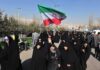 Group of women in black attire marching with an Iranian flag