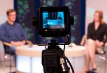 Camera focused on a television studio interview with two seated hosts