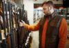 Man examining rifles in a store.