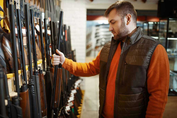 Man examining rifles in a store.