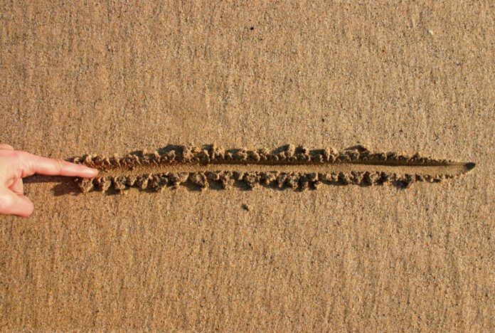 Finger drawing line in wet sand beach