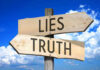 Signs pointing to Lies and Truth against sky.