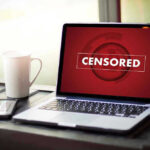 Four-Year Cover-Up EXPOSED — Feds Caught Silencing Americans Laptop screen displaying CENSORED beside coffee and phone