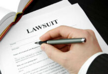 Hand holding pen, filling out lawsuit form.