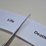 Scissors cutting a paper strip labeled 'Life' and 'Death'