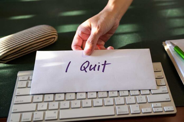 A hand placing an envelope labeled 'I Quit' on a keyboard