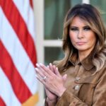 A woman in formal attire clapping in front of an American flag