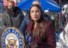 A woman speaking at a podium during a public event with a diverse audience in the background