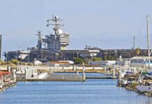A large naval aircraft carrier docked in a harbor with smaller boats in the foreground