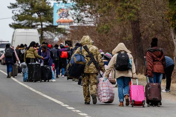 Group of people carrying luggage walking along a road with a soldier