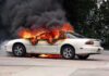 A white car engulfed in flames with thick black smoke rising