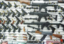 State’s SWEEPING Gun Ban TRIGGERS DOJ WAR Wall display of various firearms in a store.