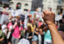 GLOBAL Protests ERUPT – UNSEEN RISKS Loom Raised fist in front of a crowd.
