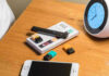 Vape pen, smartphone, clock on wooden table.