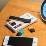 FDA’s SHOCKING Move — They Approved THAT? Vape pen, smartphone, clock on wooden table.