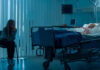 Woman sitting beside hospital bed at night.