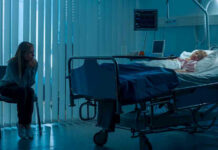 Woman sitting beside hospital bed at night.