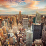 Bezos TAKES ON NYC! New York City skyline at sunset with tall buildings.