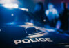 Unbelievable Charges: NFL’s STAR In Deep Trouble Police car with blurred figures in the background.