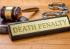 Gavel, handcuffs, and Death Penalty sign on desk.