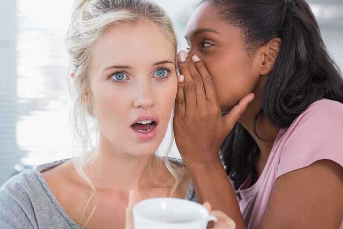shutterstock_148144184 Two women in a casual setting, one whispering to the other who looks surprised