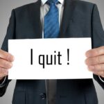 A man in a suit holding a sign that says I quit!