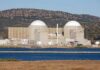 Shocking Turn: Military Stockpile Now Lighting Up Homes Nuclear power plant with domed structures beside a water body and mountains in the background