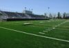 Fairness Fight Erupts: Governor Race Drawn Into Sports Battle A football field with artificial turf and empty bleachers under a clear blue sky