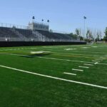 Fairness Fight Erupts: Governor Race Drawn Into Sports Battle A football field with artificial turf and empty bleachers under a clear blue sky
