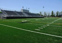 A football field with artificial turf and empty bleachers under a clear blue sky