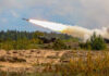 Army Plans Major Long-Range Missile Surge Military tank firing a missile in forest area.