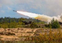 Army Plans Major Long-Range Missile Surge Military tank firing a missile in forest area.