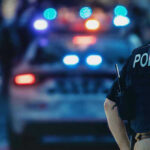 Revolving-Door Fail Exposes Pregnant Victim Police officer with patrol car and flashing lights.