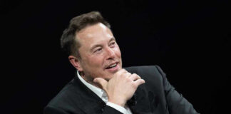 Man in suit smiling, resting chin on hand.