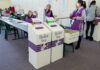 Few Cases Fuel NJ Election Debate Election polling station with ballot boxes and officials.