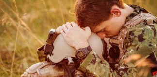 Soldier sitting, leaning head on helmet.