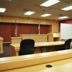Hidden in a Dryer: Teen’s Escape Exposes Alleged Predator Interior view of an empty courtroom with wooden furniture and American flags