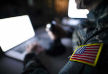 A Tiny Startup Could Help Change the Way America Fights Wars Soldier using laptop with US flag patch visible.